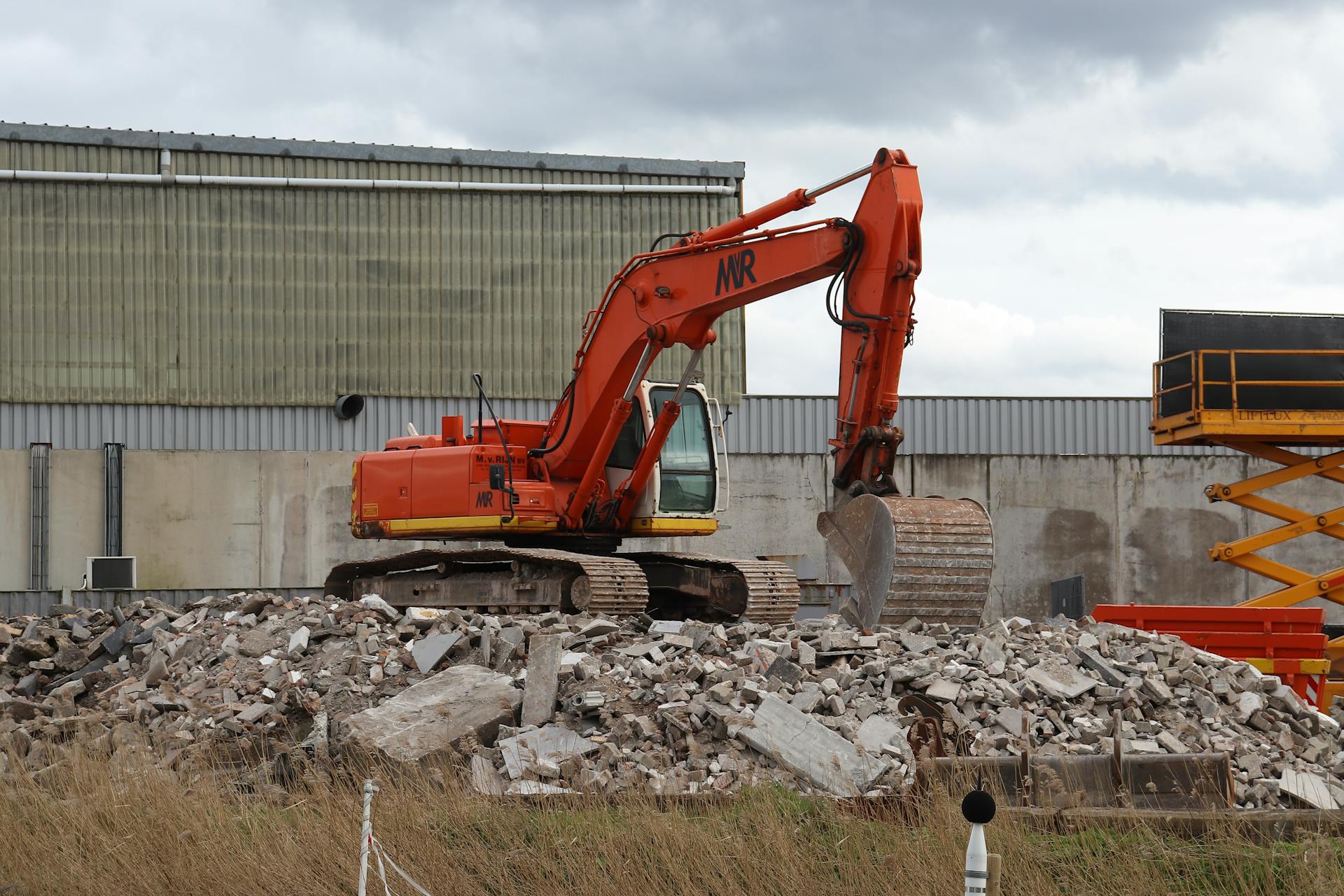 Orange excavator on a demolition site amidst rubble, showcasing construction machinery at work.