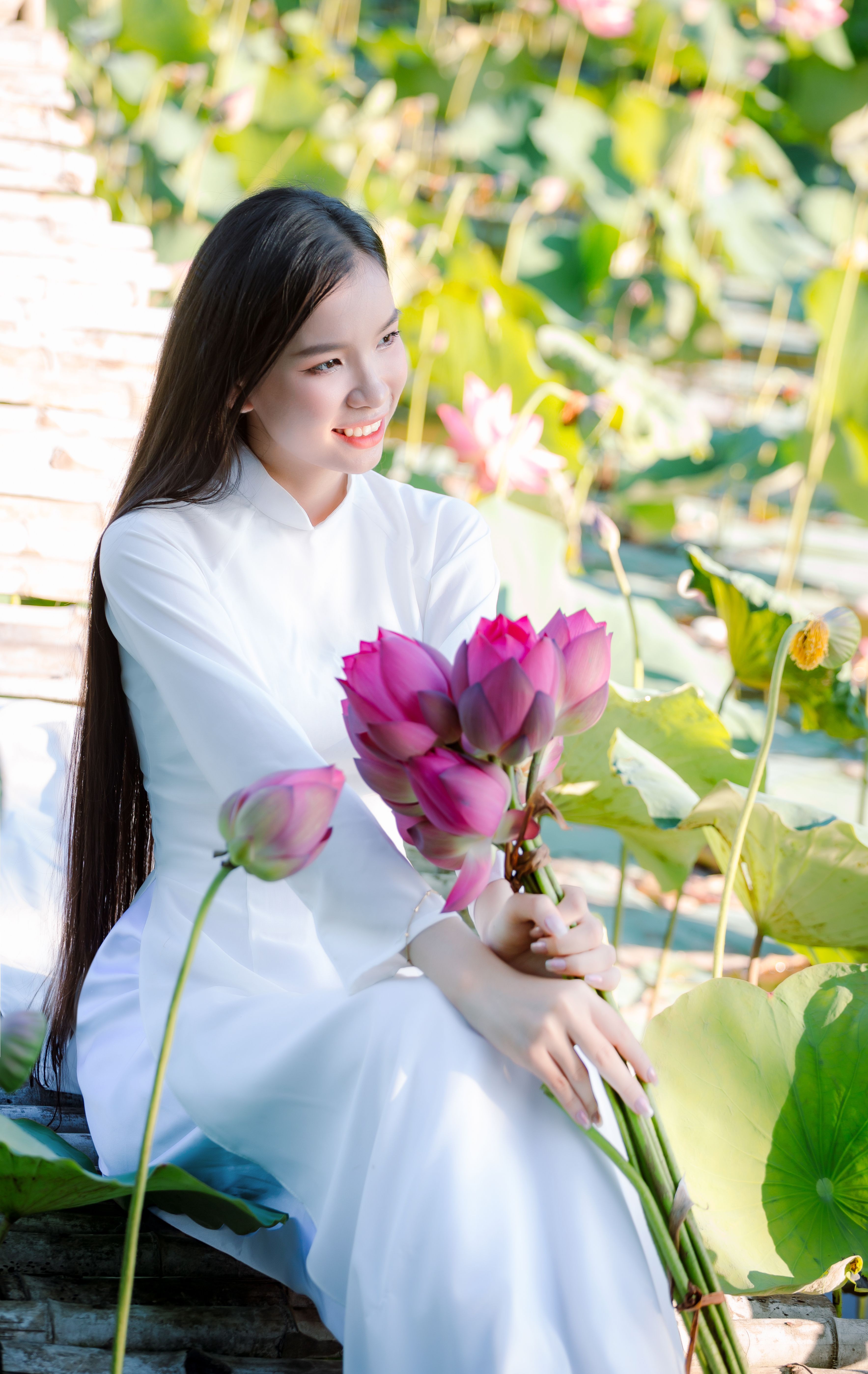 Serene woman in a traditional Vietnamese Ao Dai holding lotus flowers in Hội An.