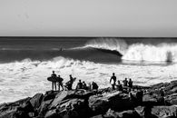 Black and white image of surfers observing waves at Taghazout beach.