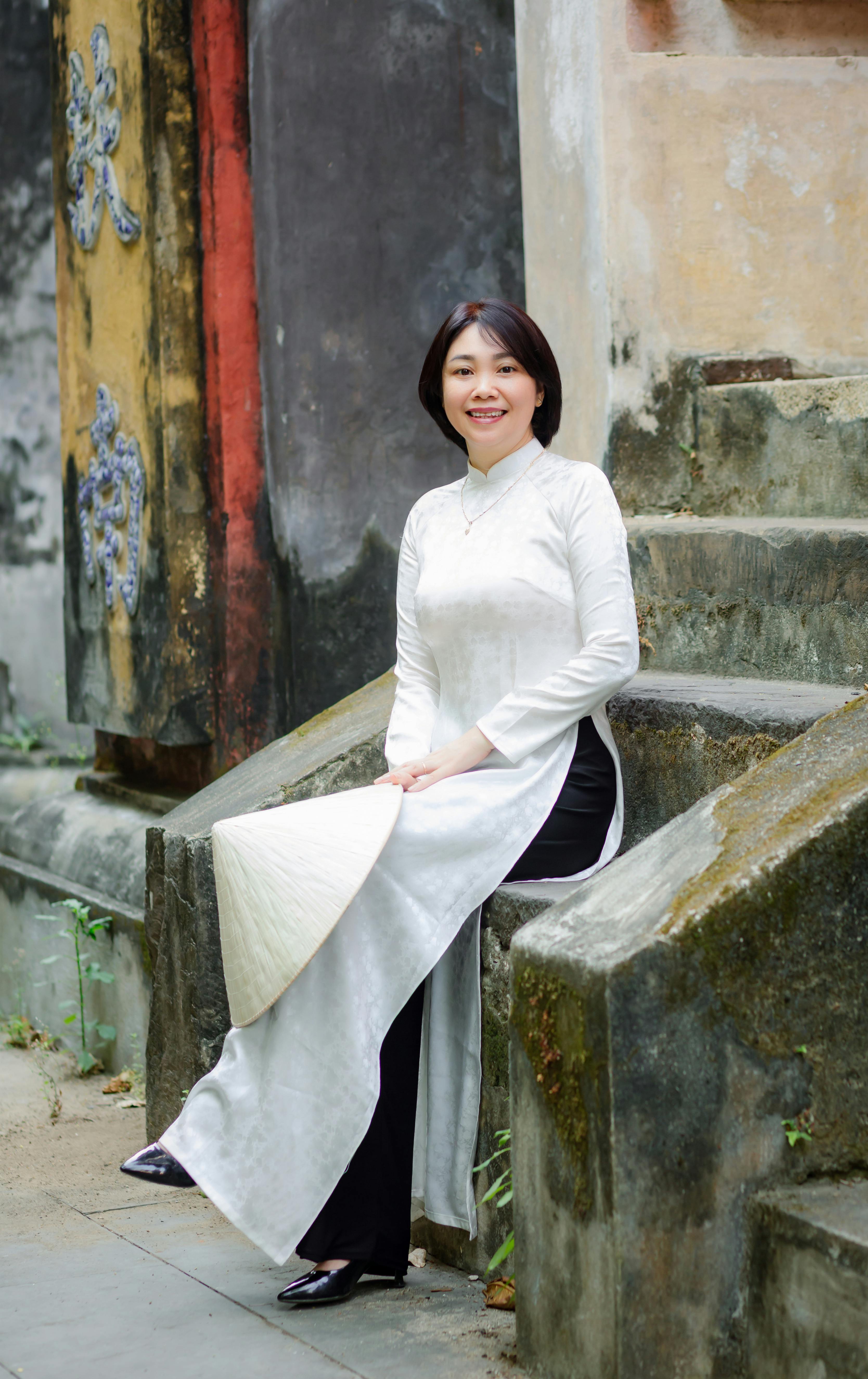 Smiling woman in traditional Ao Dai seated outdoors in Hội An, Vietnam.