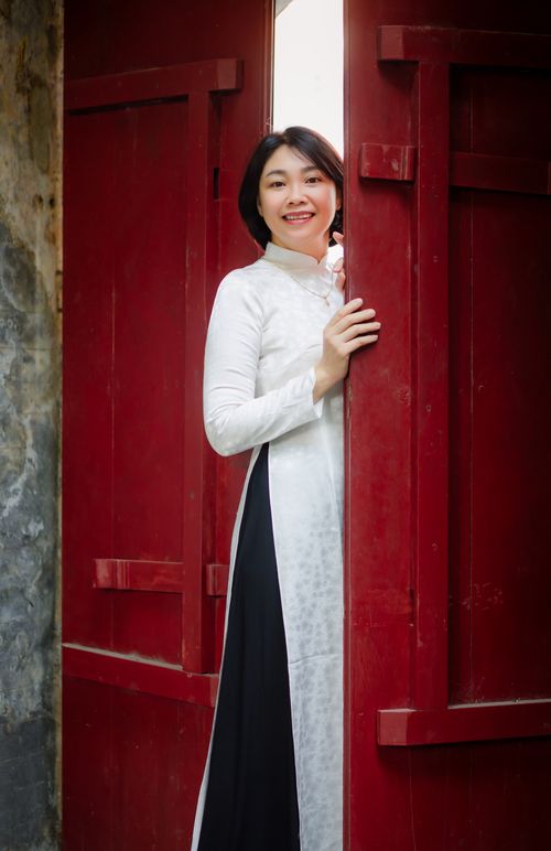 Free A woman in a traditional Vietnamese Áo Dài poses by a red door in Hội An, Vietnam. Stock Photo