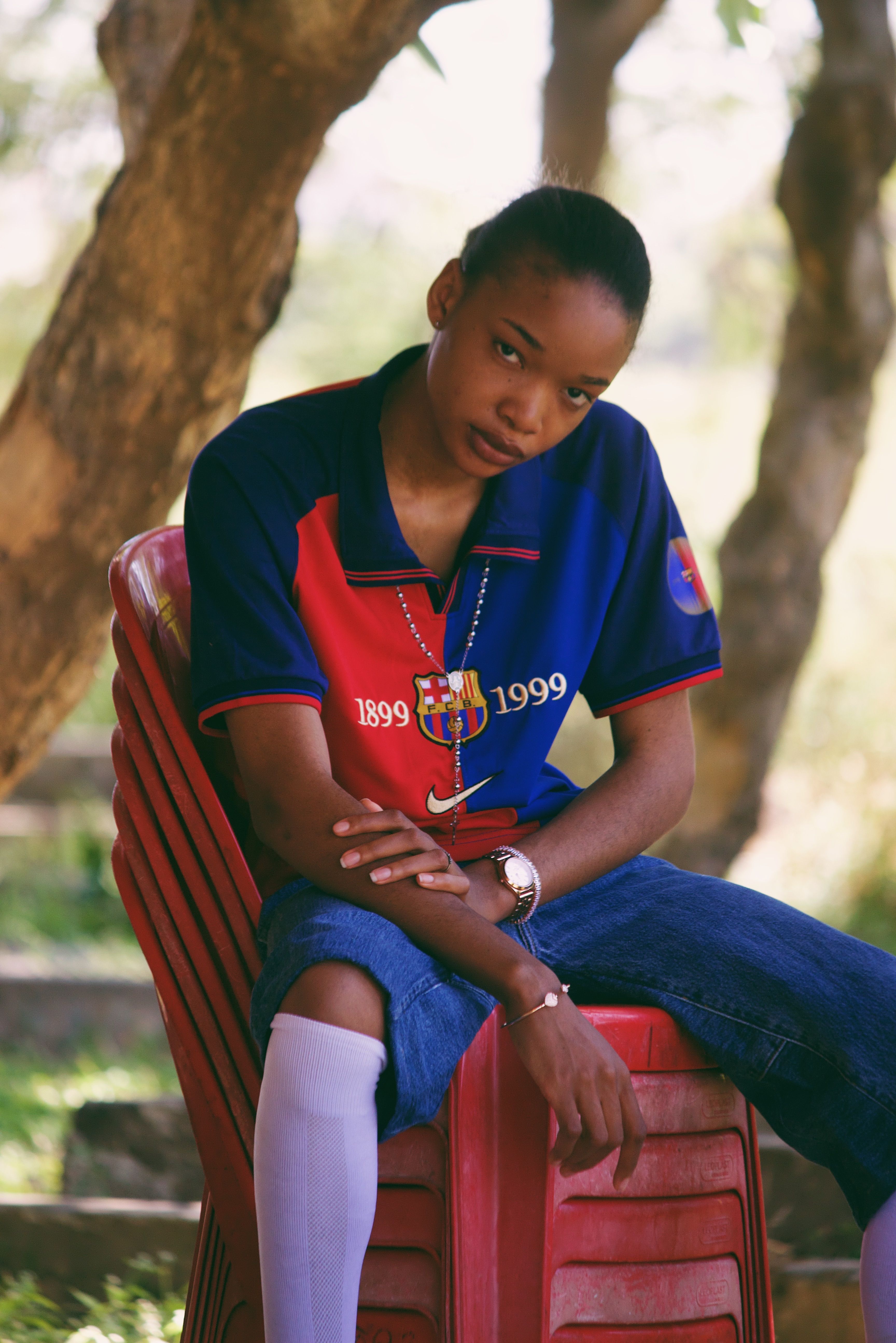 Person wearing a vintage football jersey sitting outdoors on a red chair.