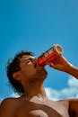 在阳光明媚的海滩日子里，男子赤裸上身，对着蓝天从罐子里喝水