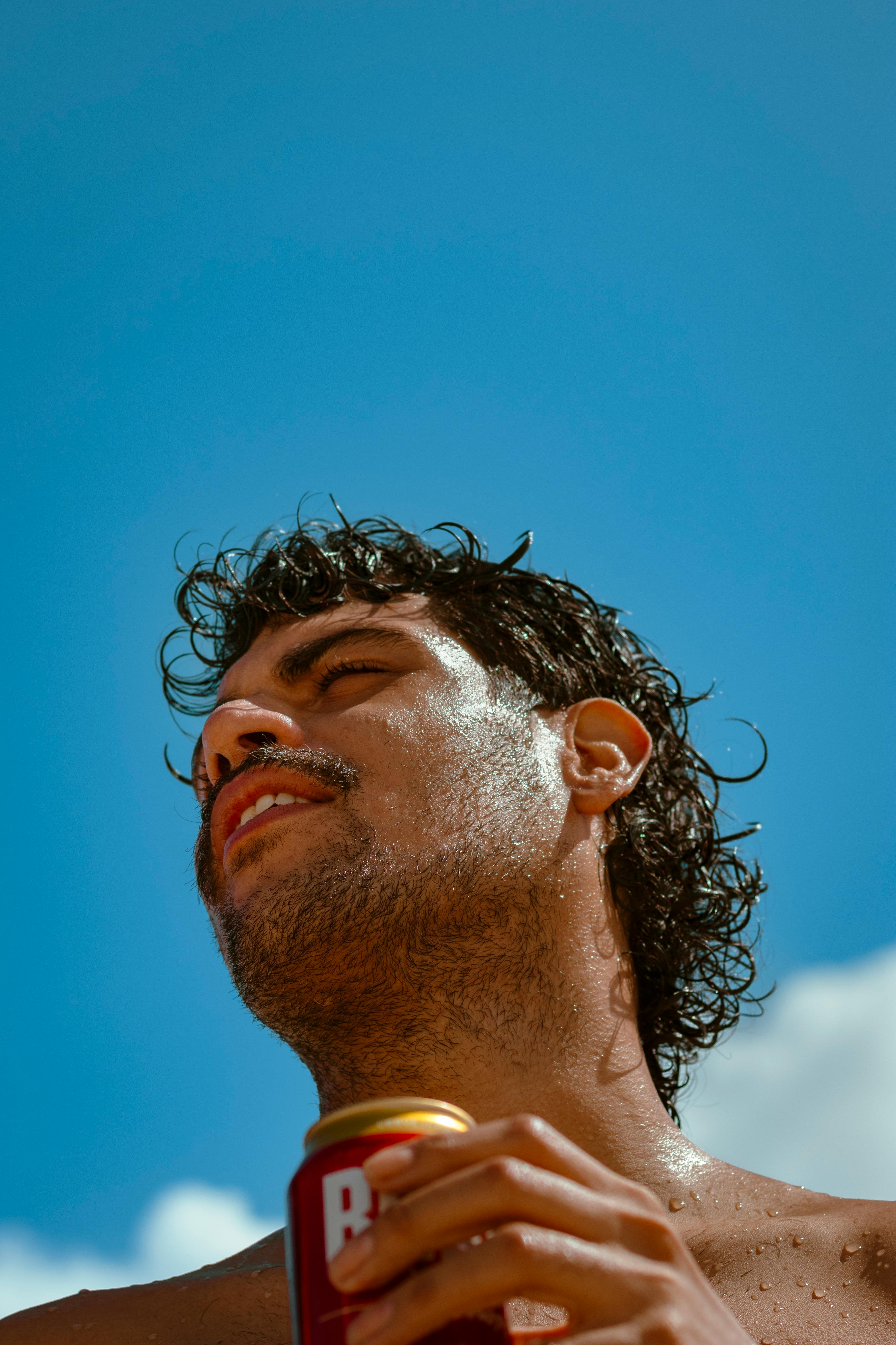 Man enjoying a refreshing drink outdoors with a bright blue sky backdrop.