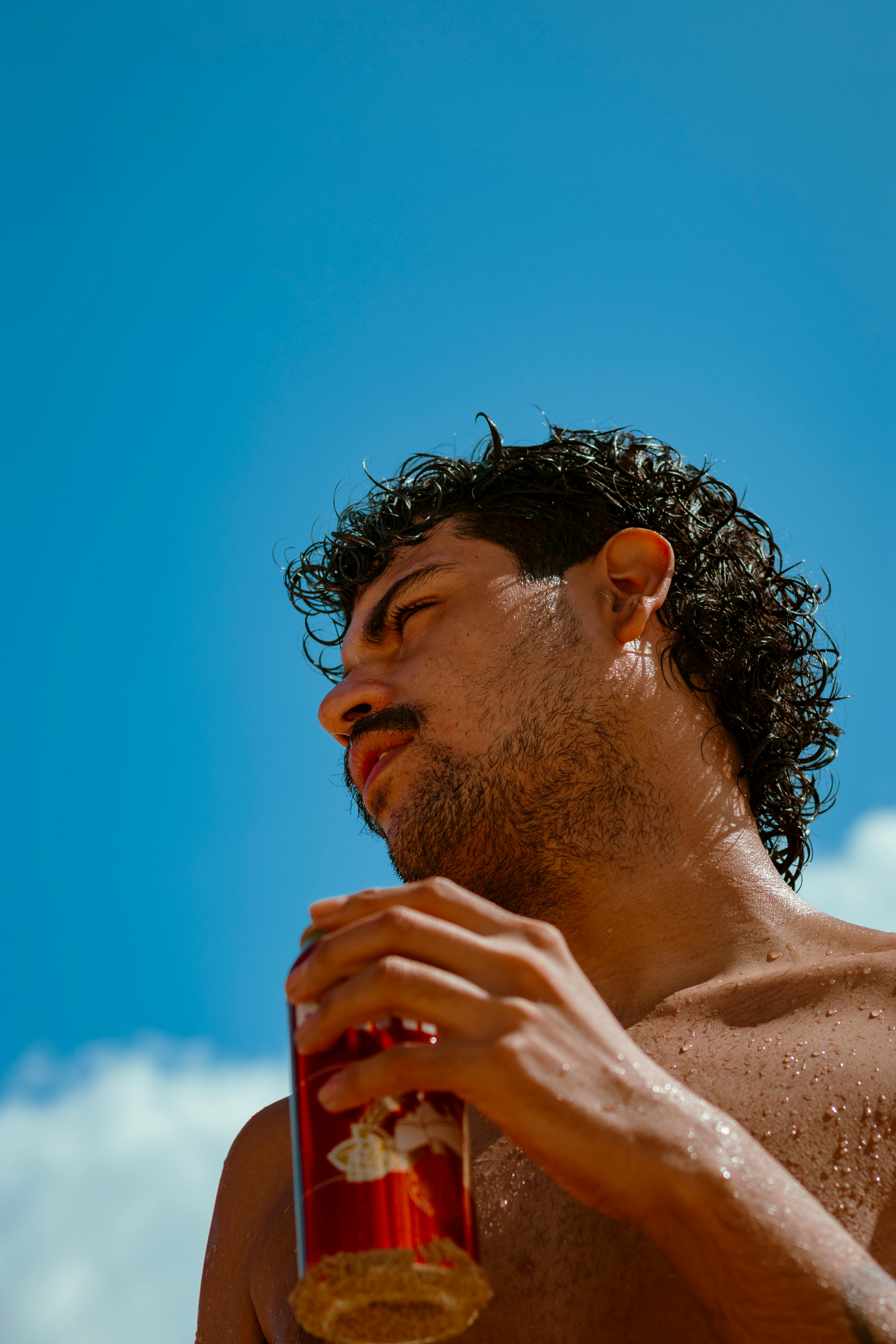Young man with a drink in hand looks towards the sky on a bright day.