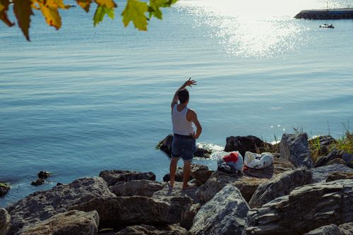 Free A man stands on rocky shore extending hand towards the sunlit sea in İstanbul. Stock Photo