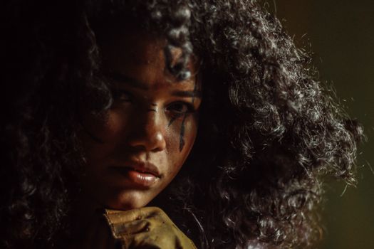 Moody portrait of a woman with curly hair and face paint, showcasing intense emotion.