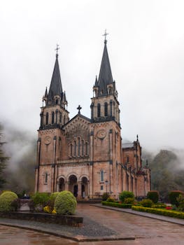 Misty view of Basilica de Covadonga, a historic landmark in Asturias, Spain, surrounded by lush greenery.