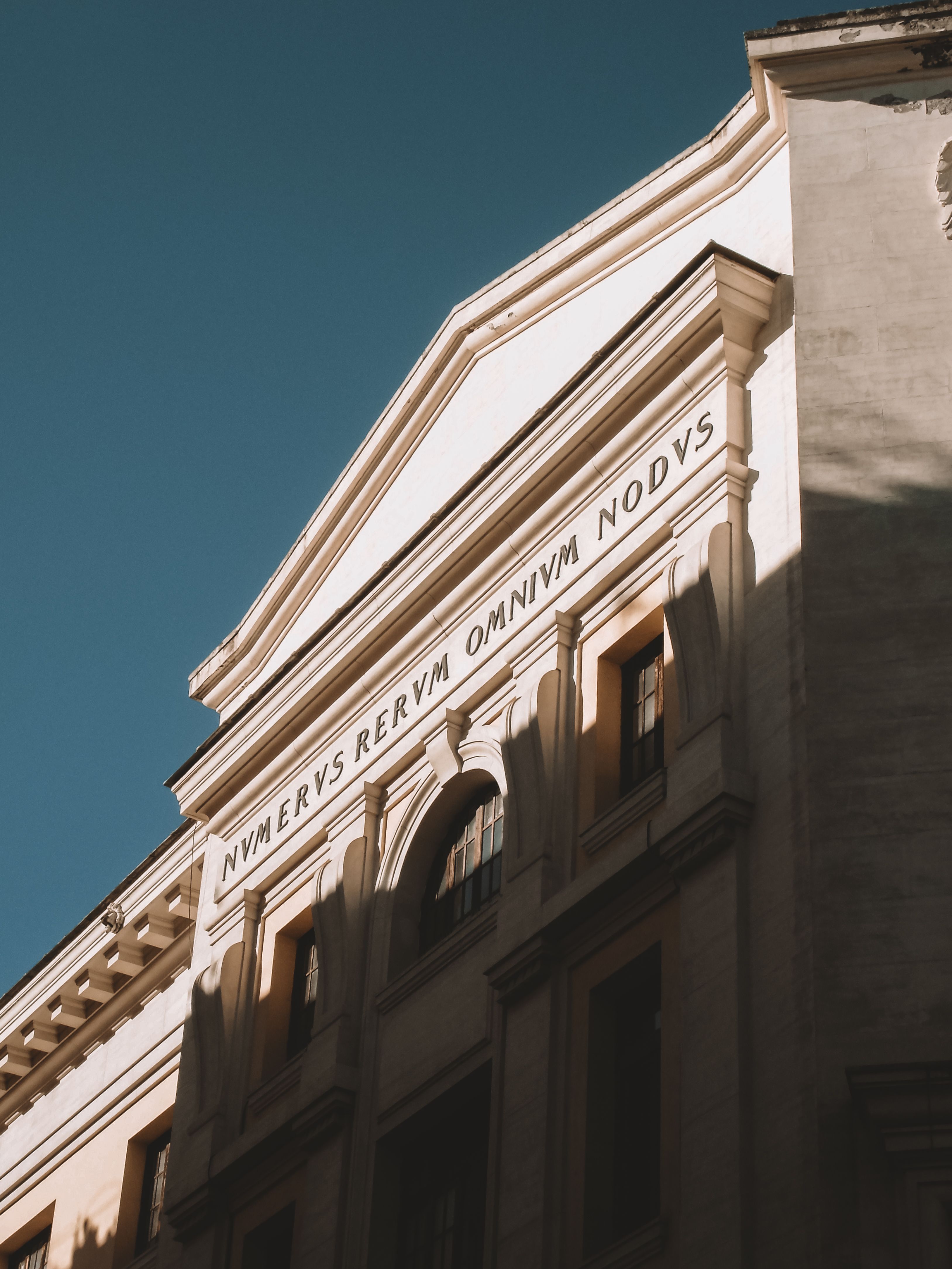 Neoclassical architectural facade in Rome featuring Latin inscription under clear sky.