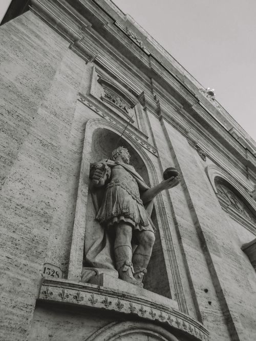 Free Black and white photo of a classical Roman sculpture on a historic building facade. Stock Photo