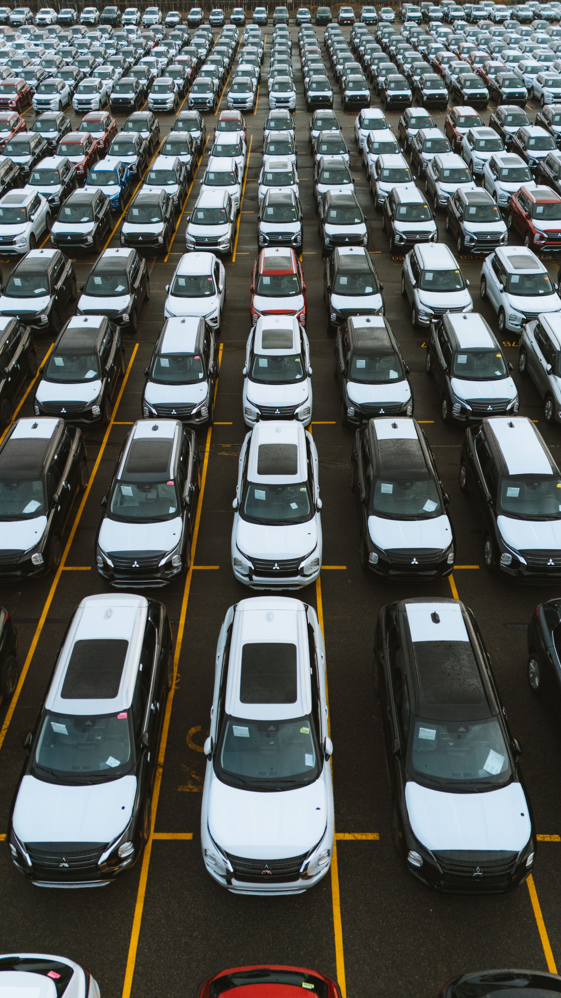 Aerial view of a large vehicle storage lot with cars arranged in parallel rows.