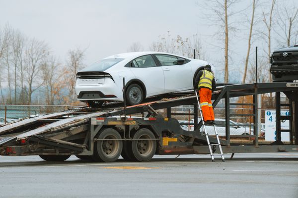Worker loading a white car onto an open auto transport trailer, showing how to ship a car when moving