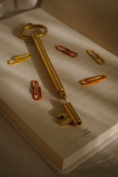 A golden key resting on an open notebook surrounded by colorful paperclips.