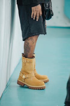 A close-up of rugged boots and tattooed legs against an aqua floor, showcasing urban fashion.