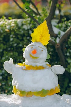 A charming snowman adorned with colorful autumn leaves in a snowy garden.