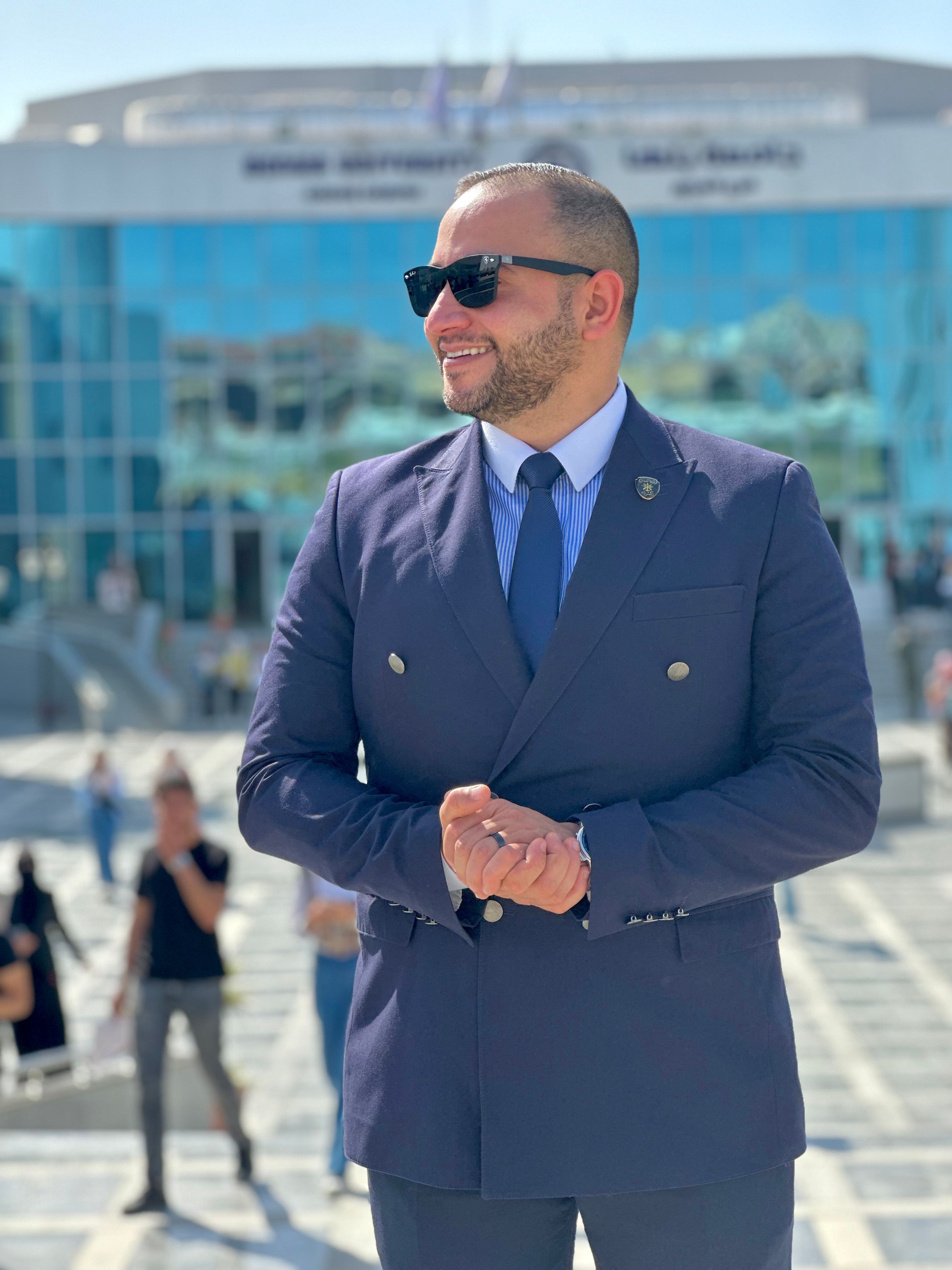 Stylish man in a suit standing outdoors in a sunny urban setting.