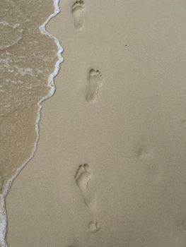 Footprints in soft sand by ocean waves, capturing a serene beach moment.