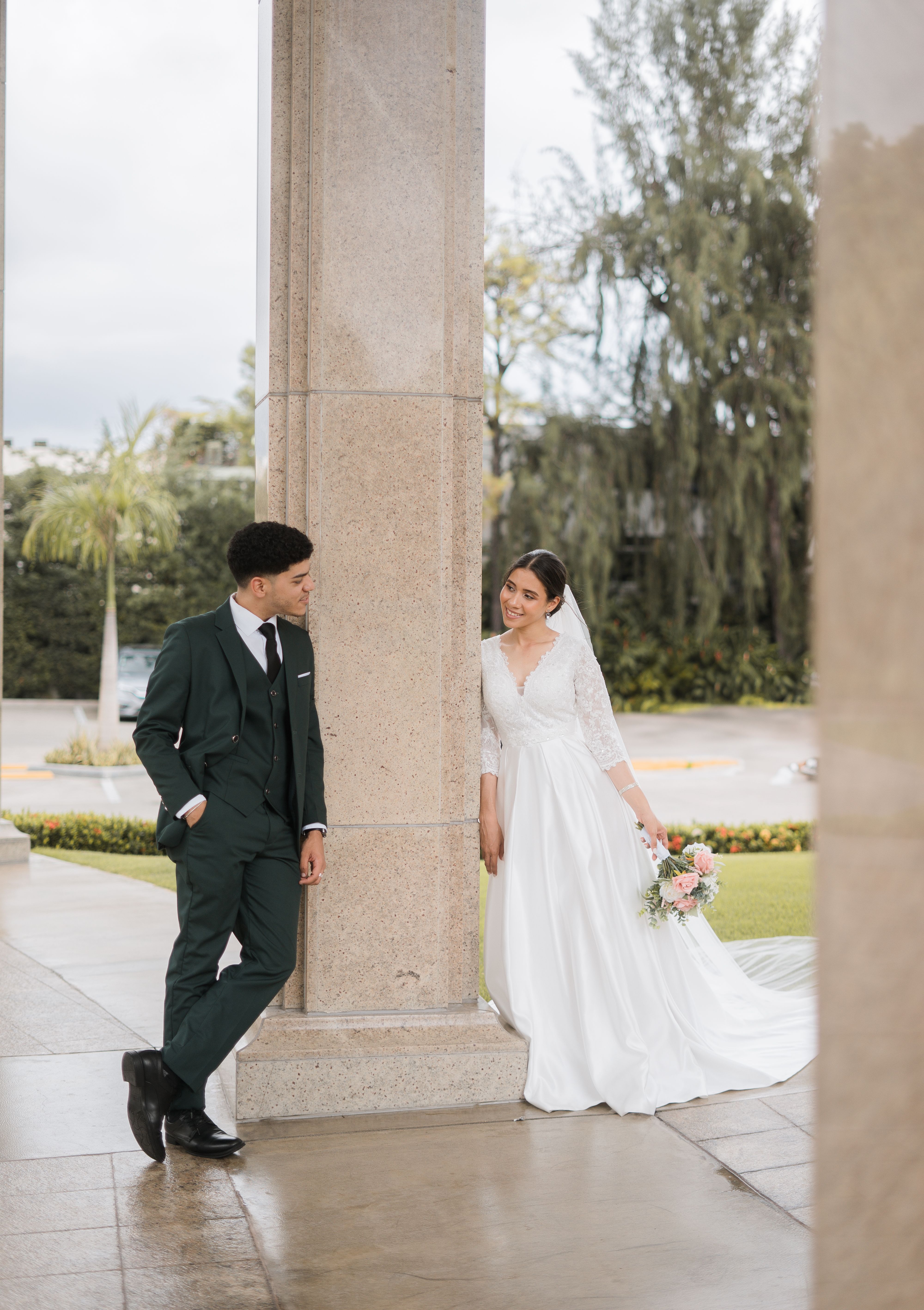 A couple in wedding attire shares a moment by a pillar in Santo Domingo.