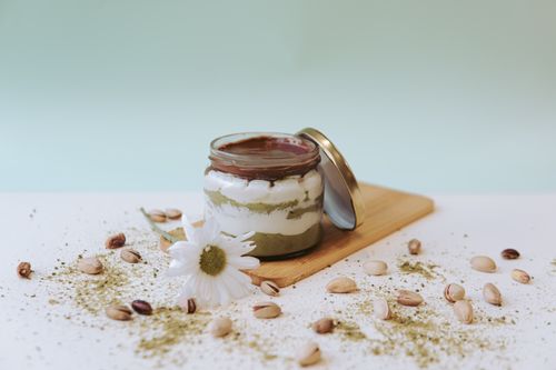 Free Layered dessert jar with chocolate, yogurt, pistachios, and chamomile decoration on wooden board. Stock Photo