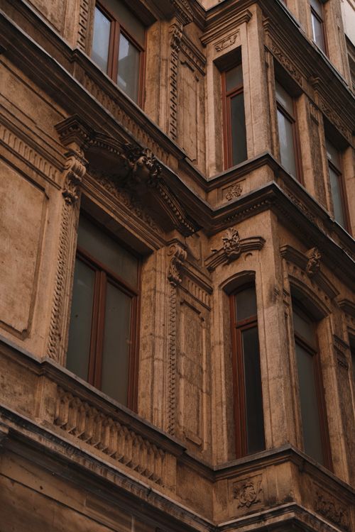 Free Detailed view of a classic stone facade with ornate architectural elements and wooden windows. Stock Photo