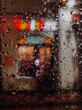 Raindrops on a window with blurred city lights creating a moody, introspective scene.