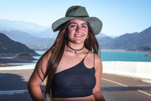 Free Smiling woman wearing sun hat and black top in front of scenic mountain view and lake. Stock Photo