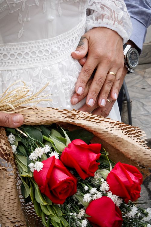 Free Close-up of hands with wedding rings and a bouquet of red roses, symbolizing love. Stock Photo