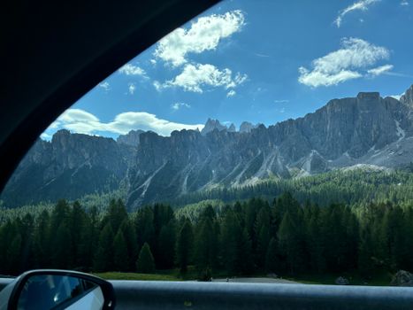Breathtaking view of the Dolomite mountains from a car window on a sunny day in Italy.