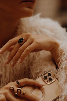 Close-up of a stylish woman's hand with rings and smartphone, in a cozy setting.