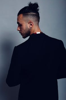 A side profile of a stylish man with a modern haircut and fashionable attire, against a neutral background.