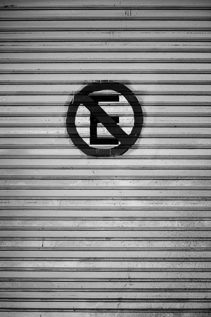 Black and white image featuring a no parking sign on a corrugated metal gate in Buenos Aires.