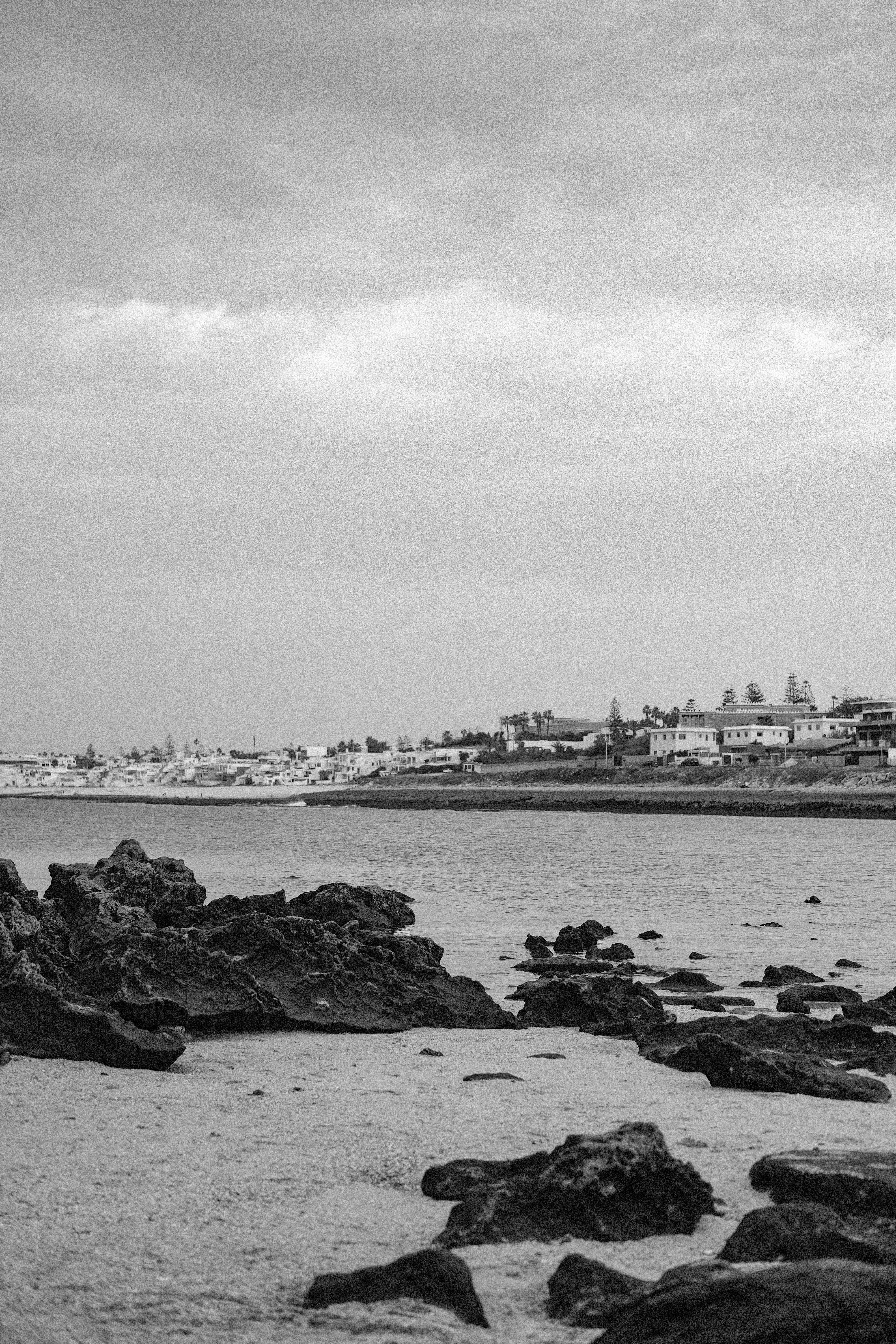 Monochrome view of Rabat's rocky coastline with cityscape in the background.