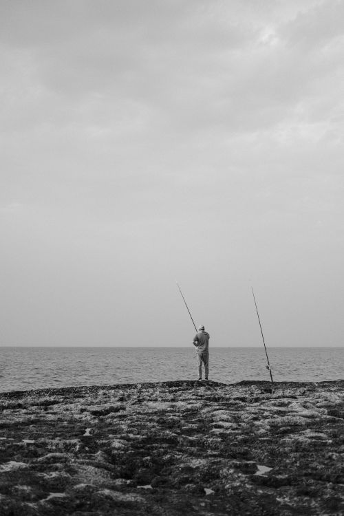 Free Black and white image of a lone fisherman by the sea in Rabat, Morocco. Stock Photo
