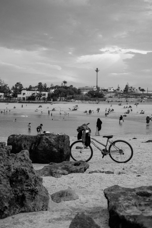 Free Black and white photograph of a beach scene with people and a bicycle in Rabat, Morocco. Stock Photo