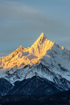 Golden sunrise illuminating a snow-covered mountain peak, creating a dramatic landscape.