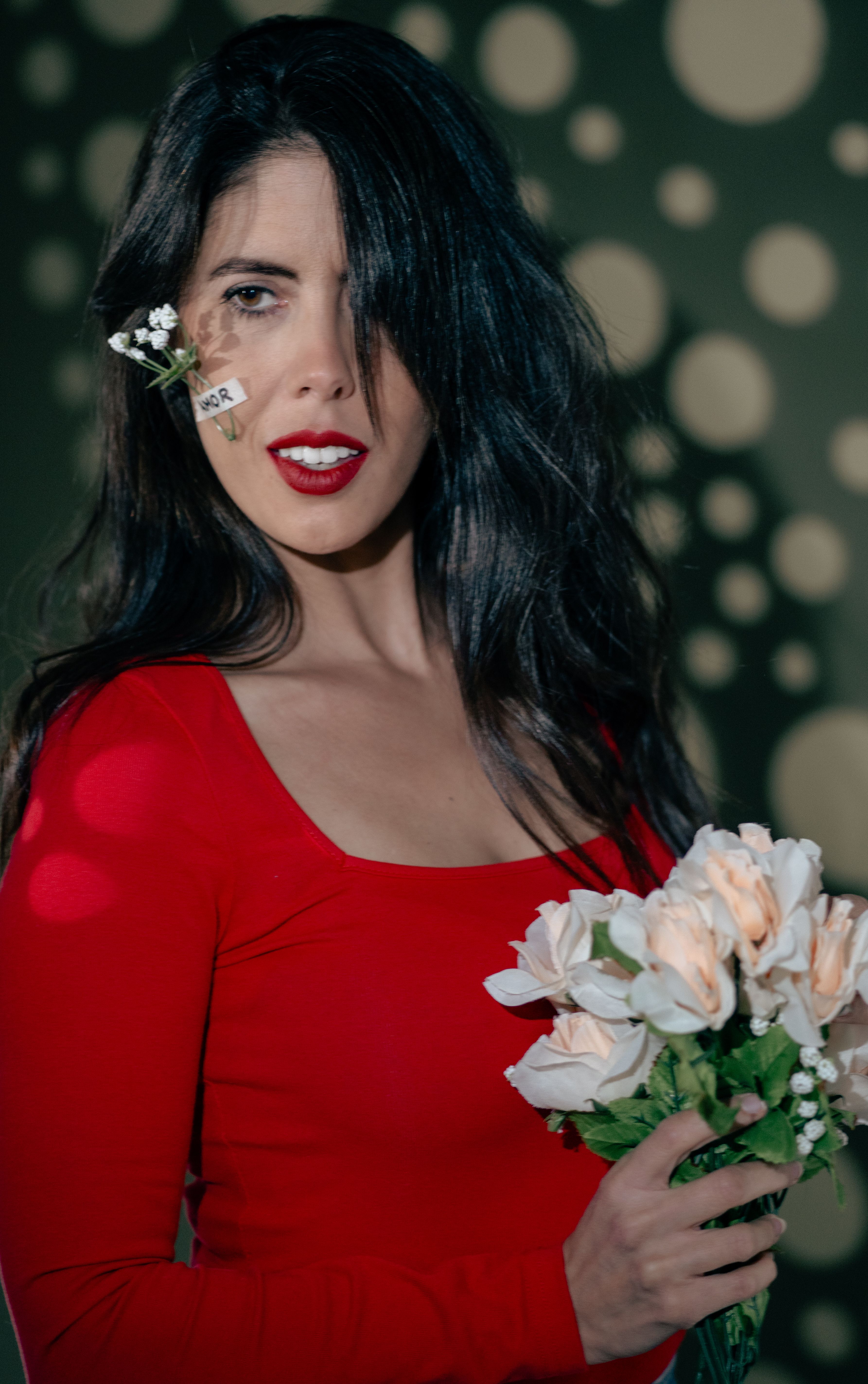Woman in a red dress with red lipstick holding white flowers indoors.