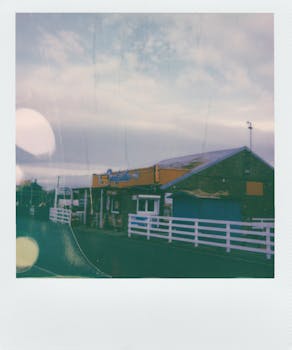 A retro-style Polaroid photograph capturing a roadside building with colorful signage under a cloudy sky.
