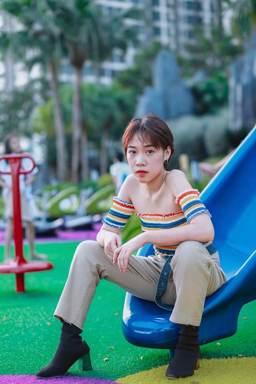 Free Young woman sitting on a playground slide with a colorful outfit and vibrant background. Stock Photo