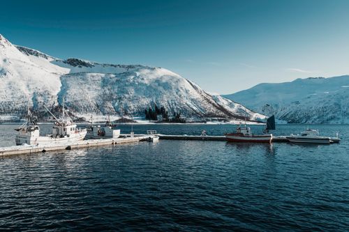 Free Beautiful Arctic harbor scene with fishing boats and snow-covered mountains in Northern Norway. Stock Photo