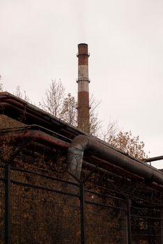 Industrial chimney emitting smoke with autumn foliage in view, symbolizing pollution.