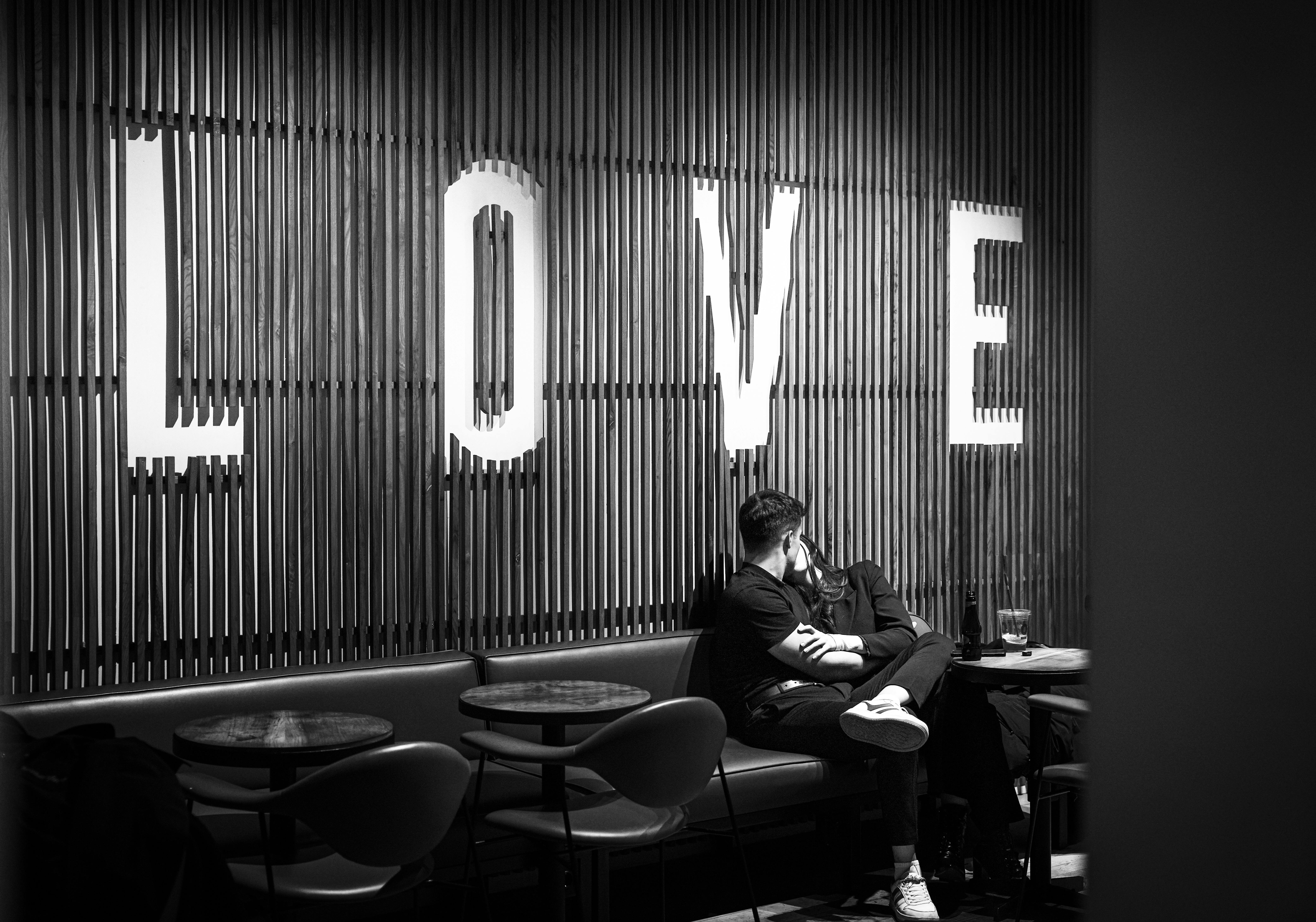 Black and white photo of a couple kissing in a café beneath a large 'LOVE' sign in Istanbul.