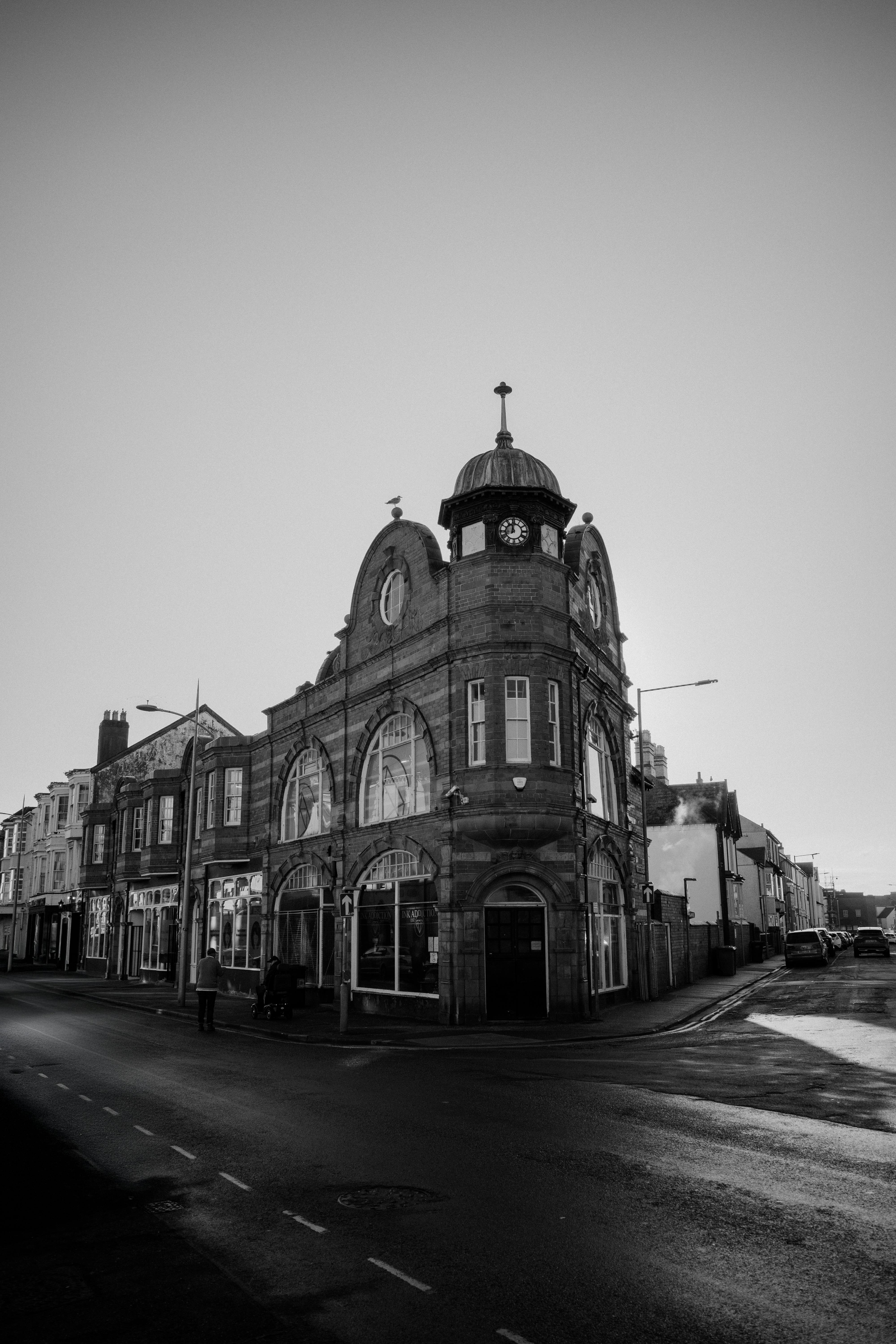 Black and white photo of an historic clock tower building on a quiet street corner.