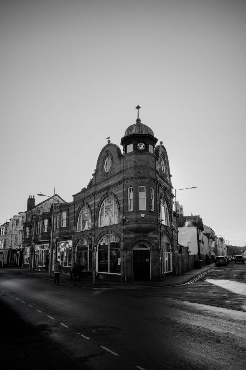 Free Black and white photo of an historic clock tower building on a quiet street corner. Stock Photo