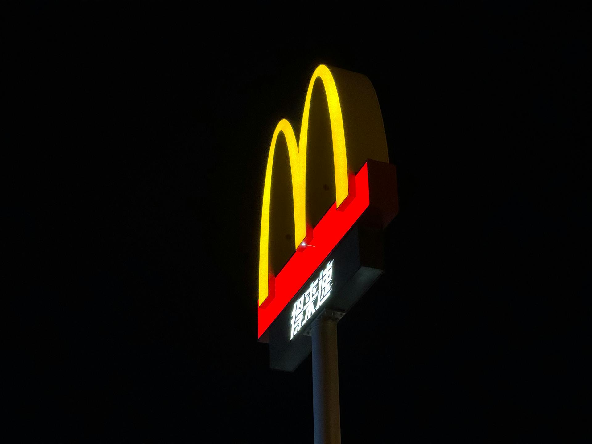 Bright McDonald's sign against a dark sky, showcasing iconic golden arches.