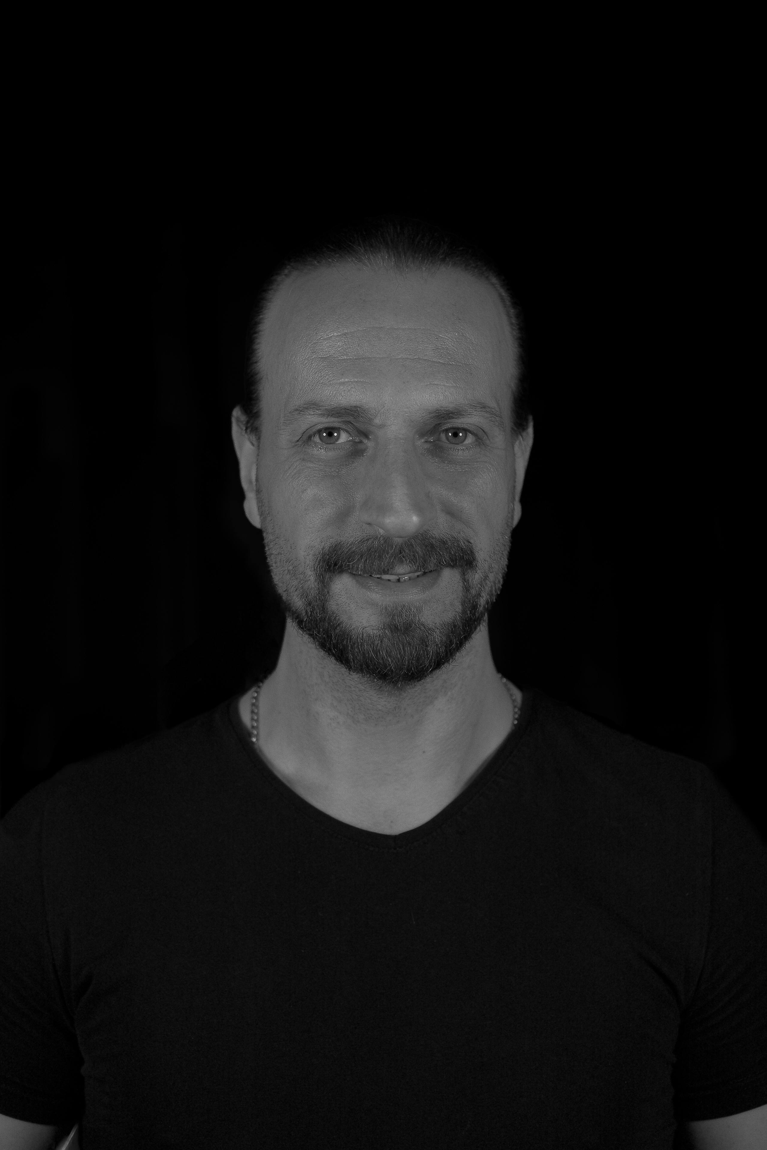 De franc Retrat en blanc i negre d'un home somrient amb barba sobre un fons fosc. Foto d'estoc