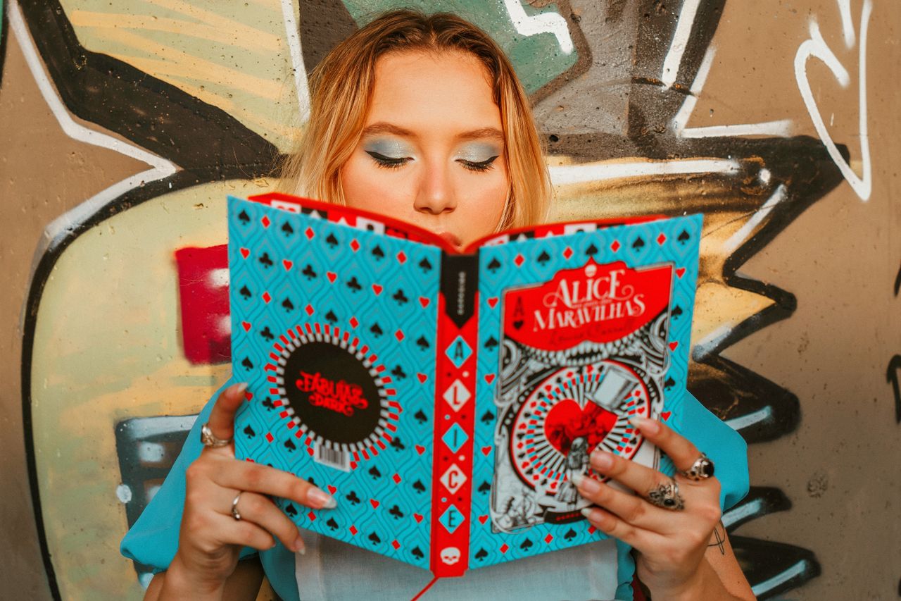 stylish young woman reading a colorful book against graffiti wall refl