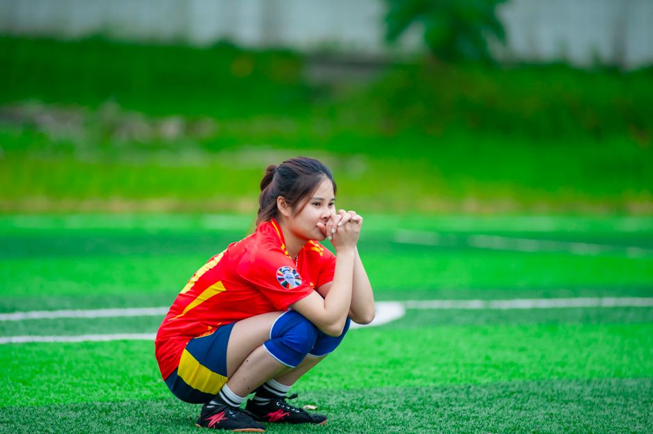 ハノイのフィールドで物思いにふける若い女性サッカー選手が、集中力と決意を示しています。