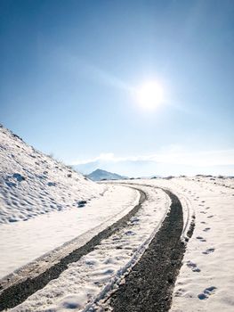 A winding road through snowy mountains under a bright sun, showcasing winter wonderland beauty.