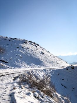 A scenic winter landscape of a snowy mountain road under a bright blue sky.