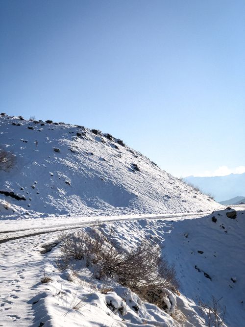 Free A scenic winter landscape of a snowy mountain road under a bright blue sky. Stock Photo